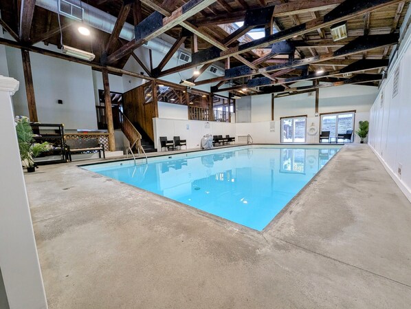 Una piscina interior con suelo de hormigón, vigas de madera y vistas al exterior a través de amplios ventanales.
