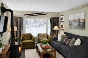 A cozy living room with a fireplace, two armchairs, a sofa, and a large window with a snowy view. - Charming Stay in Stowe Condo: Hot Tub&Indoor Pool (Stowe)
