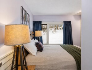 Une chambre à coucher avec un lit, deux lampes de chevet, une fenêtre avec des rideaux et une vue sur un paysage enneigé.
