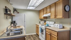 A kitchen with wooden cabinets, a microwave, a toaster, and a refrigerator. - Charming Stay in Stowe Condo: Hot Tub&Indoor Pool (Stowe)