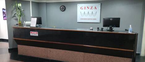 A reception desk with a sign reading "GINZA CONDOMINIO EDIFÍCIO GINZA" and a clock on the wall.