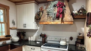 A kitchen with white cabinets, a stove, and a window. - Adirondack Cabin (Schroon Lake)