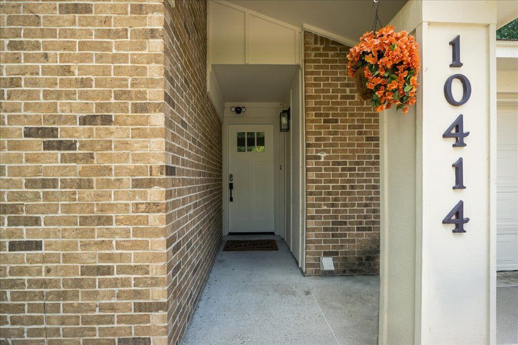 Un bâtiment en briques avec une porte blanche et un panier à fleurs suspendu.
