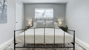 A bedroom with a bed, two bedside tables, a ceiling fan, a window with blinds, and a door. - NEW Charming 3BR 2BA w/Modern Fireplace by Domain @ Q2 Stadium (Austin)