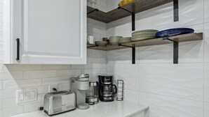 A kitchen with white subway tiles, a toaster, a coffee maker, and wooden shelves holding plates and bowls. - NEW Charming 3BR 2BA w/Modern Fireplace by Domain @ Q2 Stadium (Austin)