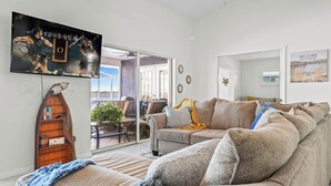 A living room with a large flat-screen TV, a wooden boat decoration, a sofa, and a view of the outdoors. - On LAKE JUNE (Lake Placid)