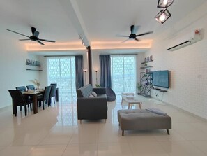 Ein modernes Wohnzimmer mit Essbereich, zwei Deckenventilatoren, einem Flachbildfernseher und einer weißen Ziegelwand.