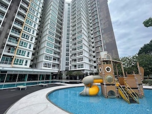 A modern high-rise building with a swimming pool and a children's play structure.