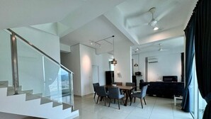 Ein modernes Wohnzimmer mit einer Glastreppe, einem Essbereich mit Tisch und Stühlen sowie einer Küchenzeile mit dunkler Arbeitsplatte und Geräten.