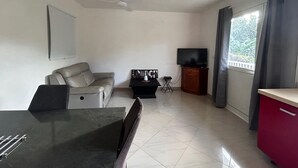A modern living room with a sofa, a dining table, a TV, and a balcony with curtains.