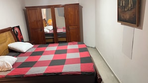 A bedroom with a checkered bedspread, wooden wardrobe, and a painting on the wall.