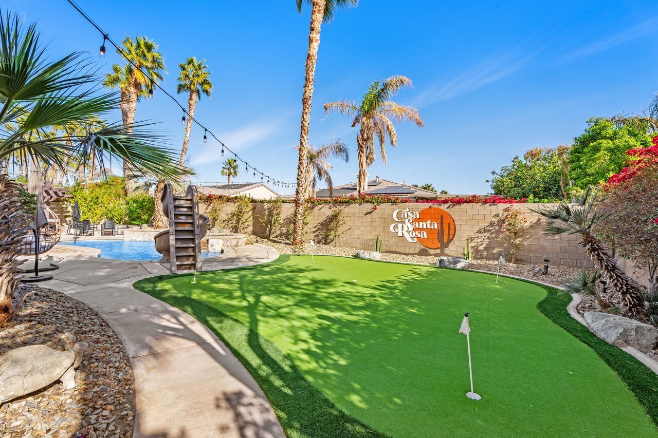 Een golfbaan met een putting green, palmbomen en een bakstenen muur met de tekst 'Casa Santa Rosa'.