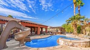 Una piscina con tobogán, sillones de descanso y un jacuzzi.