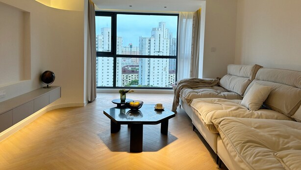 A modern living room with a large window, a sofa, a coffee table, and a small round mirror on a cabinet. - Eastern Hub - Superior 3bedroom Near TianZiFang&XinTianDi, Near Subway (shanghai)