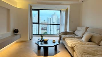 A modern living room with a large window, a sofa, a coffee table, and a small round mirror on a cabinet.