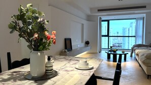A modern living room with a dining area, featuring a marble table, a vase with flowers, and a large window offering a city view. - Eastern Hub - Superior 3bedroom Near TianZiFang&XinTianDi, Near Subway (shanghai)