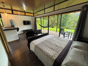 Une chambre dotée d’un grand lit, d’un bureau, d’une télévision et offrant une vue sur un jardin grâce à de grandes fenêtres.