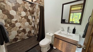 Un baño con ducha, inodoro, lavabo y espejo.