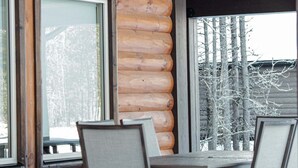 A log cabin with a dining area featuring a table and chairs, large windows, and a view of trees.