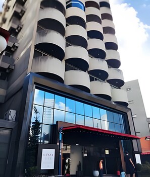 Ein modernes Gebäude mit einer Reihe zylindrischer Elemente an der Fassade, einem großen Glasvordereingang und einer roten Markise vor dem Eingang.