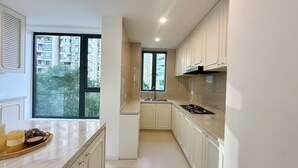 Una cucina moderna con mobili bianchi, un fornello e un lavello. Si vede una finestra con vista su edifici e alberi.