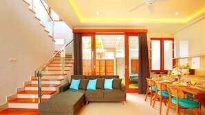 A modern living room with a sectional sofa, a dining area with wooden chairs, and a staircase with glass railings. - Luxury Villa Noam 2BR Nusa Dua (Nusa Dua)
