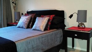Een keurig opgemaakt slaapkamer met een bed, twee nachtkastjes, een lamp en een vaas met gedroogde bloemen.