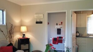 Een woonkamer met een bank, een lamp, een klein tafeltje met een plant, en een keuken die zichtbaar is door een open deur.
