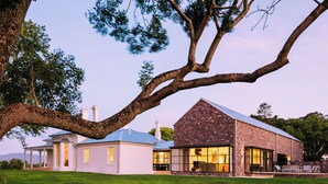 A large house with a brick exterior, a large tree in the foreground, and a grassy lawn. - Leighton House, an unforgettable luxury farm stay in Northern Tasmania, Evandale (Western Junction)