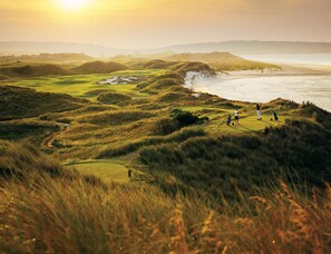 Un parcours de golf offrant une vue sur l’océan et les collines lointaines.