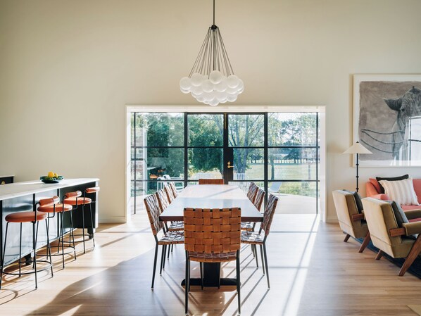 Un vaste espace dédié à la salle à manger, avec une longue table et des chaises, de grandes fenêtres et un luminaire suspendu moderne.