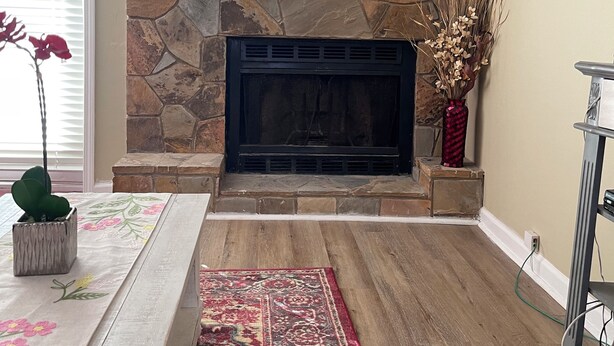 A living room with a stone fireplace, a wooden floor, a red rug, and a floral table runner. - Charming 3-bedroom house with WiFi, AC in welcoming Conyers (Conyers)