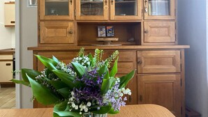Un meuble en bois avec des portes en verre, un vase rempli de fleurs et un livre intitulé « Hunger Games » sur l’étagère.