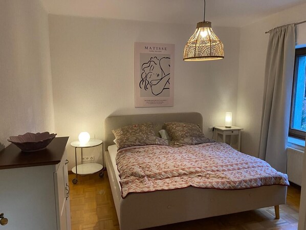 A bedroom with a bed, bedside lamps, a wall-mounted light fixture, a poster, and a window with curtains.