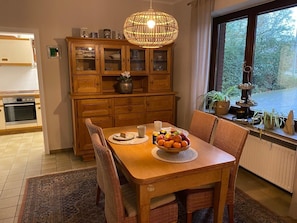 A dining area with a wooden table, chairs, a fruit bowl, and a hanging light fixture.