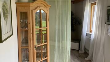 Un mobile in legno con ante in vetro, una pianta verde sopra e una tenda leggera.