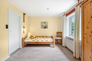 Une chambre à coucher avec un lit en bois, une chaise, une fenêtre avec des rideaux, un radiateur et un tableau accroché au mur.