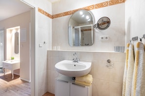 A bathroom with a sink, mirror, towel rack, and a shower area.