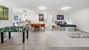 A modern living room with a foosball table, a dining area, a sofa, and a bed.