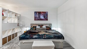 A modern bedroom with a bed, a white wardrobe, a bench, and a forest-themed wall art.
