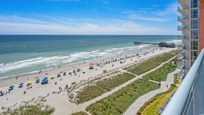 A beach with umbrellas, a pier, and a building with balconies overlooking the ocean. - Oceanfront- 2BR  2BA  beautiful condo in the heart of Myrtle Beach (Myrtle Beach)