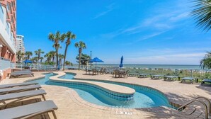 A pool area with lounge chairs and umbrellas, a curved pool, and a view of the ocean. - Oceanfront- 2BR  2BA  beautiful condo in the heart of Myrtle Beach (Myrtle Beach)