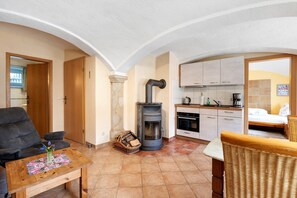 A cozy living area with a sofa, a wooden coffee table, a wicker chair, a fireplace, a kitchen with cabinets, and a bed with a pillow. - Holiday Apartment '2' with Shared Terrace, Shared Garden and Wi-Fi (Hohnstein)