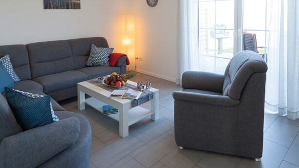 A living room with a grey sofa, a white coffee table with a fruit bowl, a grey armchair, and a large window with curtains. - Holiday Home 'Brise' with Private Terrace, Shared Garden and Wi-Fi (Boren)