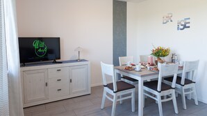 A dining area with a table, chairs, a television, and a cabinet. - Holiday Home 'Brise' with Private Terrace, Shared Garden and Wi-Fi (Boren)