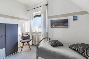 A bedroom with a bed, a chair, a wardrobe, a window with curtains, and a painting on the wall.