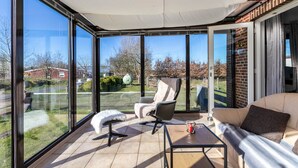 Un solárium con ventanas amplias, un sillón acolchado, un sofá y una mesita.