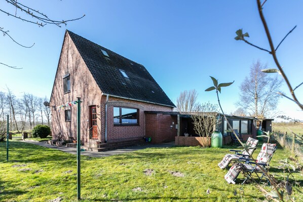 A brick house with a sloped roof, a small attached structure, and a grassy yard with outdoor furniture.