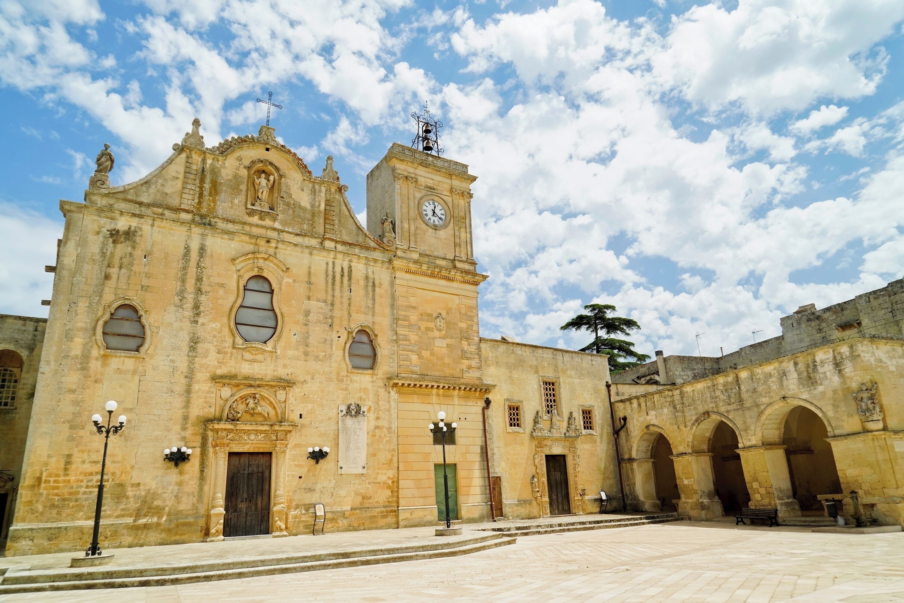 A historic building with a clock tower, arched doorways, and a courtyard.
