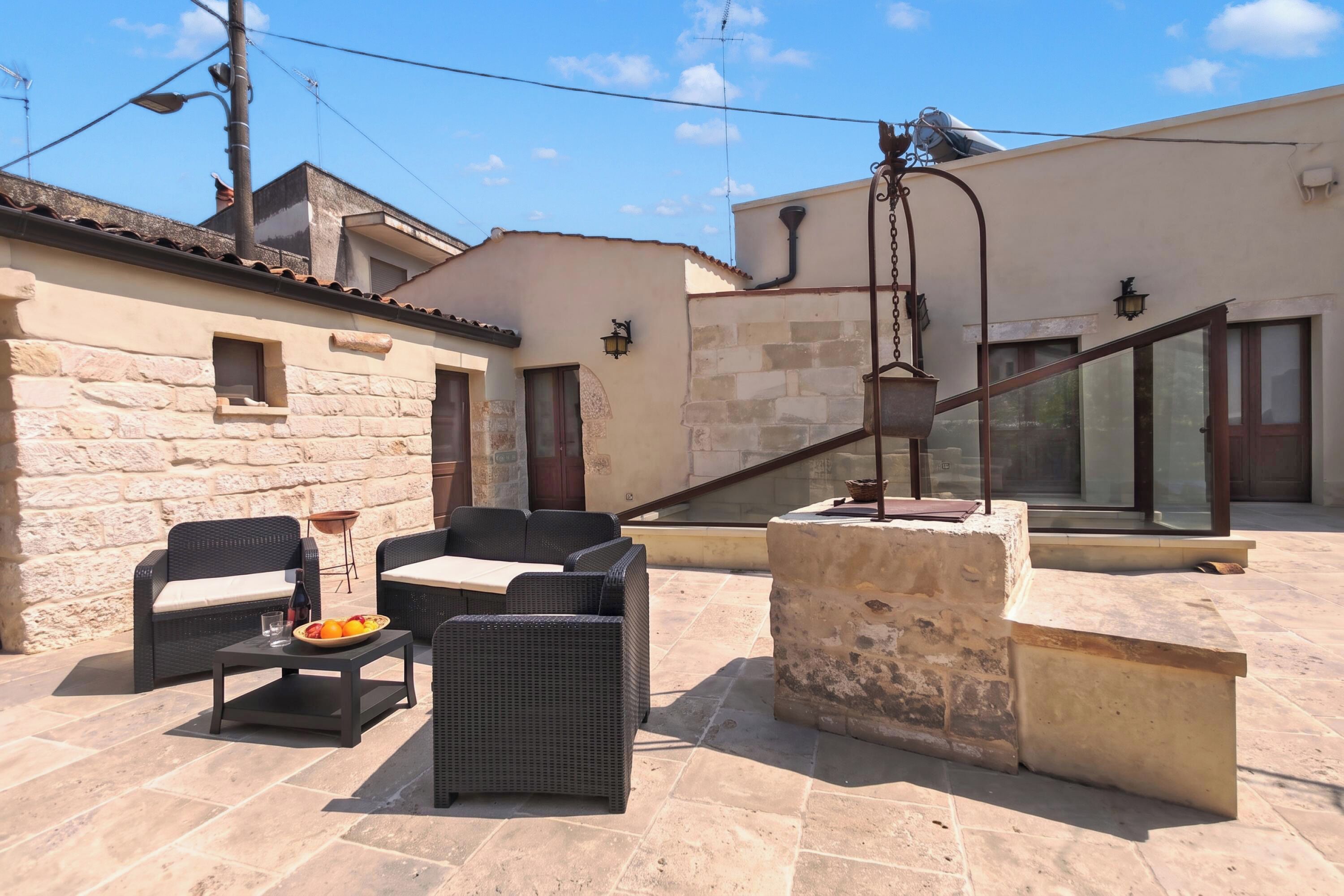 An outdoor patio with wicker furniture, a stone table, and a view of the surrounding buildings.